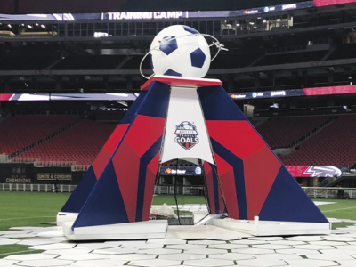 Large foam sculptures of large goalie gloves and sponsorship logos at a soccer field.